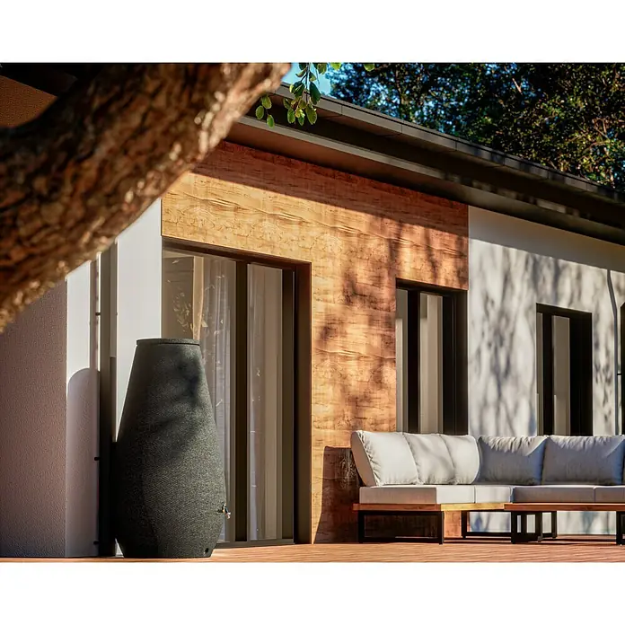 Arves Regenspeicher Drop - 410 l, Anthrazit, 1 Stk. - Diese Nahaufnahme zeigt eine stilvolle graue Regentonnen neben einer modernen Terrasse mit hellen Gartenmöbeln und Holzelementen.