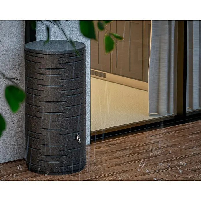 Arves Regenspeicher Freze - 410 l, Granit - Ein Regenfass in Holzoptik steht auf einer Holzterrasse, während es regnet. Das Fass hat einen Hahn und ist von Blättern umgeben.