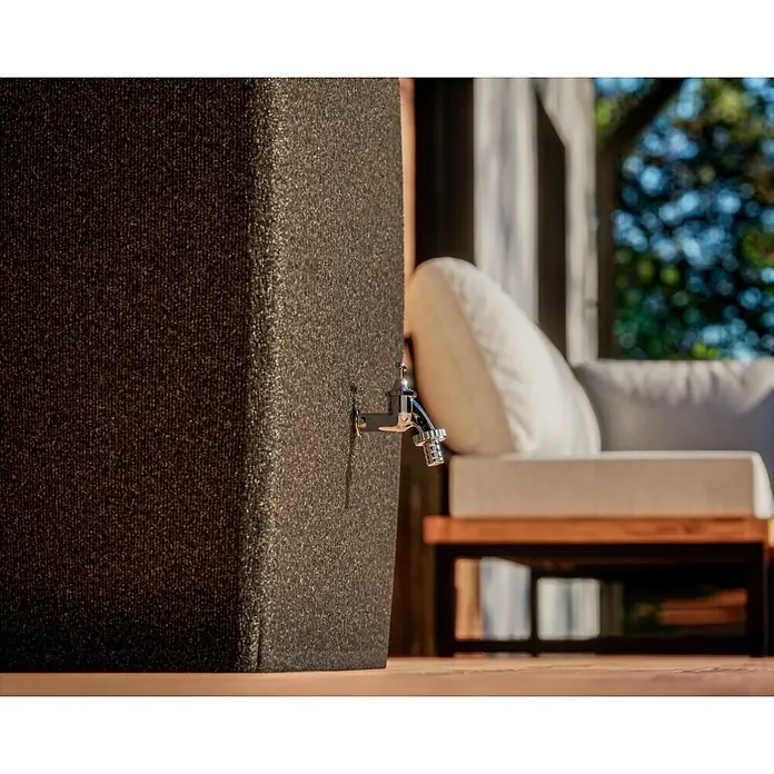 Arves Regenspeicher Boxy - 720 l, Granitkörnung, 1 Stk. - Nahaufnahme eines Regentonnenhahns an einer Regentonne, mit einem verschwommenen Hintergrund eines Sitzbereichs im Freien.