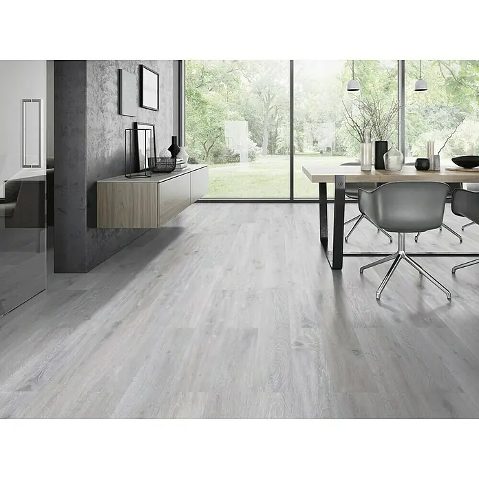 Classen Vinylbodenmuster GreenVinyl Eiche gekalkt Grau - 300 x 173 x 4 mm, Landhausdiele - Ein heller Raum mit grauem Holzboden, Esstisch und Stühlen. Der Holzboden verleiht dem Raum eine moderne und elegante Atmosphäre.