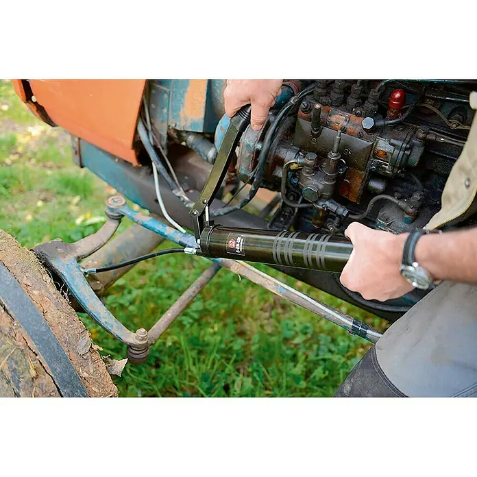 3 en 1 Bomba manual - Apto para: Cartuchos de grasa convencionales - Aquí hay una pistola de engrase en acción, esencial para el mantenimiento de maquinaria y equipos agrícolas.