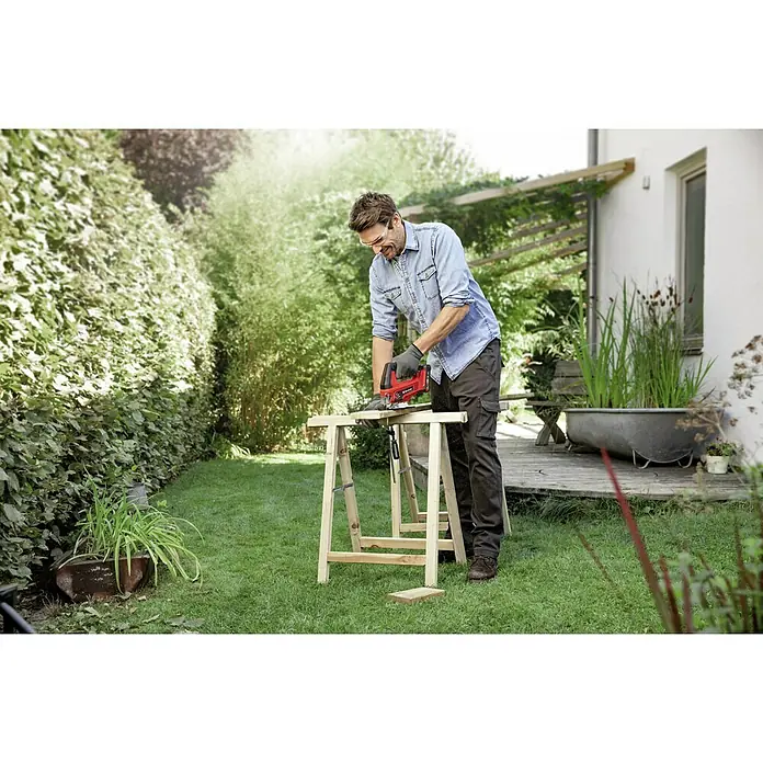 Einhell Power X-Change 18V Akku-Pendelhubstichsäge TC-JS 18 Li-Solo - 18 V, Ohne Akku, 0 /min - 2.700 /min - Ein Mann arbeitet mit einer roten Einhell Stichsäge im Garten an einem Holzbock. Er trägt Handschuhe und eine Jeansjacke.