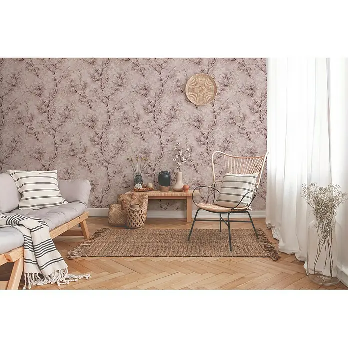 A.S. Création New Walls Vliestapete Bäume - Rosa, Floral, 10,05 x 0,53 m - Wohnzimmer mit einem hellen Sofa, einem geflochtenen Stuhl, einem Holztisch und einem gewebten Teppich auf einem Fischgrätenparkettboden.