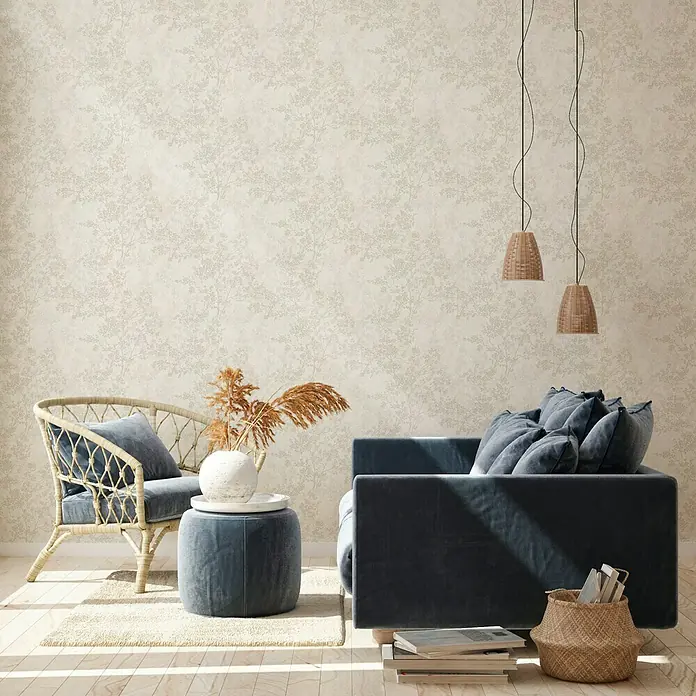 A.S. Création New Walls Vliestapete Bäume - Creme, Floral, 10,05 x 0,53 m - Eine moderne Wohnzimmerszene mit einem blauen Sofa, einem Rattansessel und dekorativen Elementen vor einer floralen Tapete.