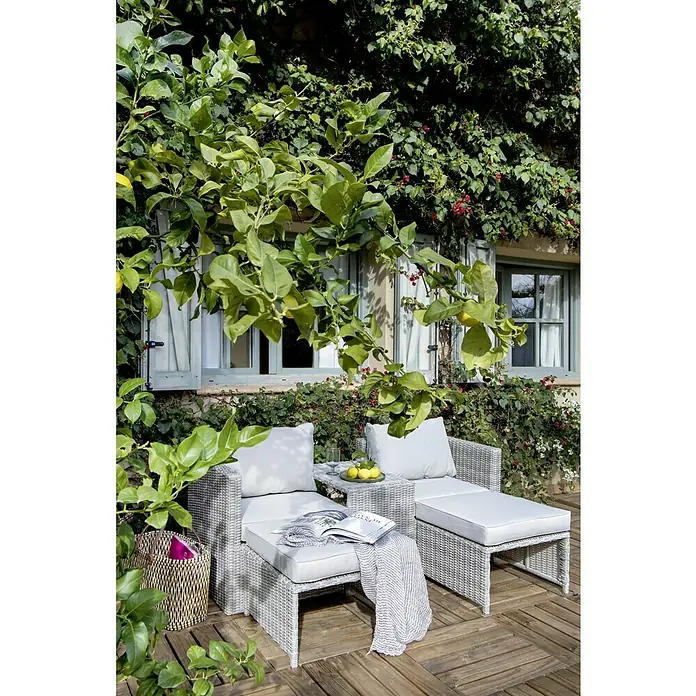 Conjunto de muebles Delma - 5 pzs., Ratán sintético, Gris - Juego de muebles de exterior con sofá de ratán gris claro, otomana y mesa con limones bajo un árbol.