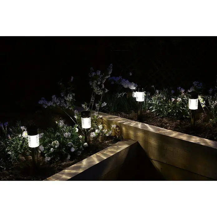 Luxform Solar-Erdspieß Rennes - Transparent, Schwarz, 5 lm - Nachtaufnahme von vier Solarleuchten im Garten, die ein warmes Licht auf Pflanzen und Holzeinfassungen werfen.