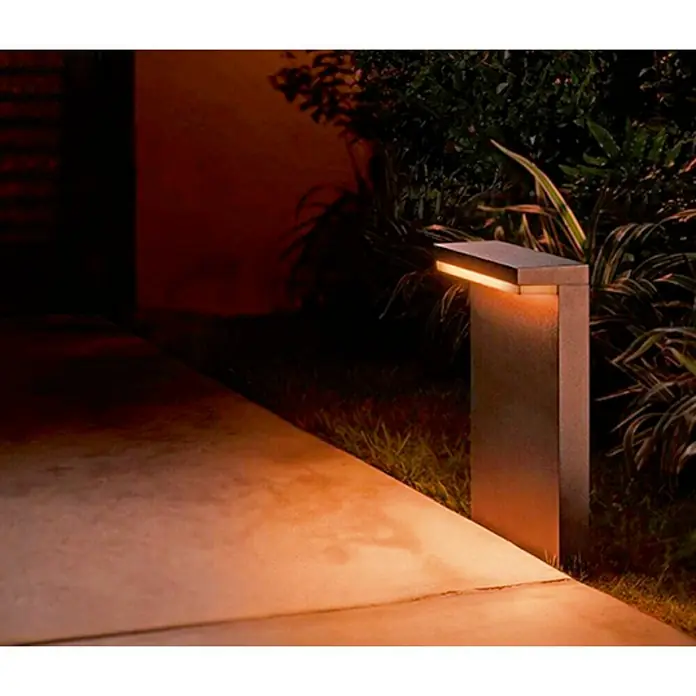 Philips Hue Sobremuro exterior Nyro - 13,5 W, Color del marco: Negro, RGBW, 9,9 x 25,5 x 40 cm, Con bombillas - Una luz exterior elegante y moderna ilumina un camino con luz cálida, creando un ambiente acogedor en el jardín.