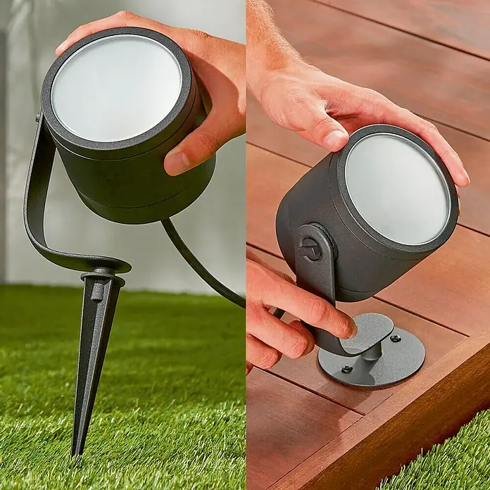 Philips Hue LED-Gartenspot Lily - Höhe: 19 cm - Ein vielseitiger, schwarzer Gartenstrahler, der sowohl in den Boden gesteckt als auch auf Holz montiert werden kann, wird von Händen gehalten.