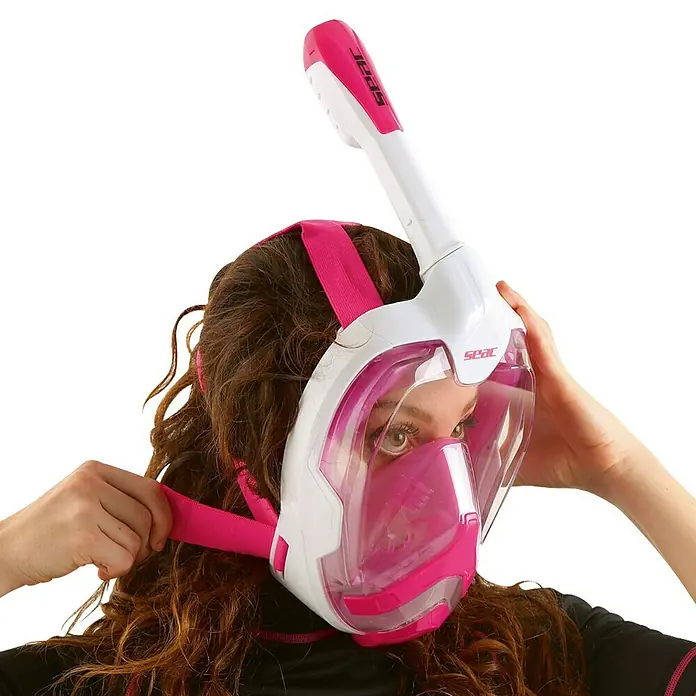 Seac Sub Máscara de Snorkel Magica - S/M, Plástico, Rosa - Una mujer se ajusta una máscara de esnórquel facial completa SEAC rosa, ideal para una visión submarina clara y una respiración cómoda.