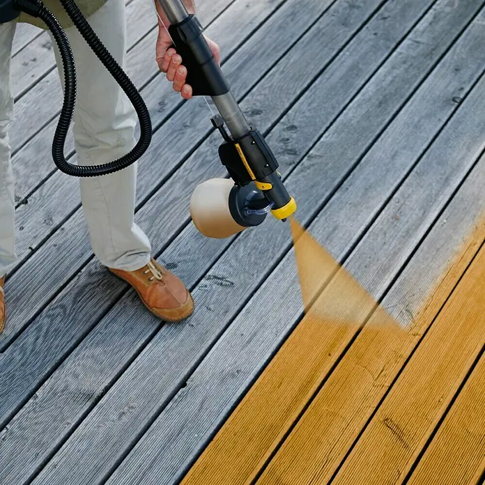 Wagner Griffverlängerung Universal EXTRA Extension - Länge: 60 cm - Eine Person behandelt eine Holzterrasse mit einem Farbsprühgerät, das die Dielen mit einem satten Farbton versieht.