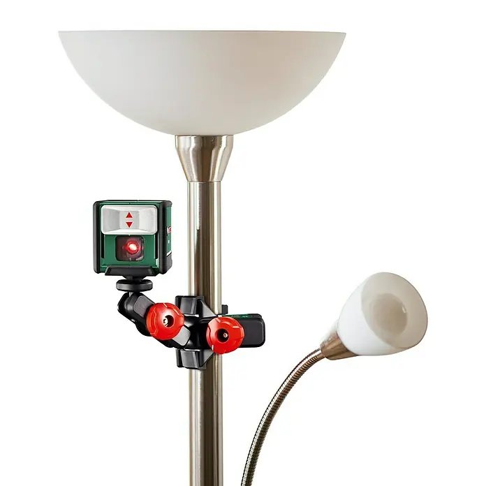 Bosch Nivel láser en cruz Quigo - Zona de trabajo máx.: 10 m, Ángulo líneas láser: 90 ° - Un láser de líneas cruzadas Bosch Quigo Green está fijado a una lámpara de pie, ideal para una alineación precisa en proyectos de bricolaje.