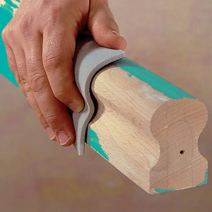 Wolfcraft Schleifschwamm-Set - 3 -tlg. - Nahaufnahme einer Hand, die ein Werkzeug zum Reinigen einer geformten Holzoberfläche mit Farbresten verwendet.