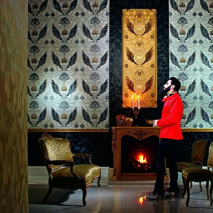 Glööckler Vliestapete - Silber, Ornament, 10,05 x 0,7 m - Ein opulent dekorierter Raum mit auffälliger Tapete, goldenen Akzenten und einem Mann in roter Jacke.