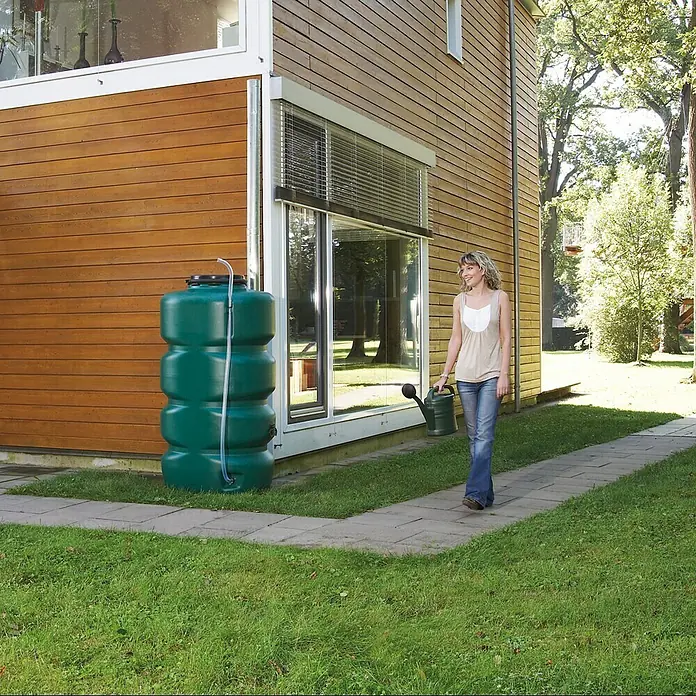Garantia Basic Line Regentonne - 500 l, Grün - Eine grüne Regentonne neben einem modernen Haus, eine Frau gießt Pflanzen.