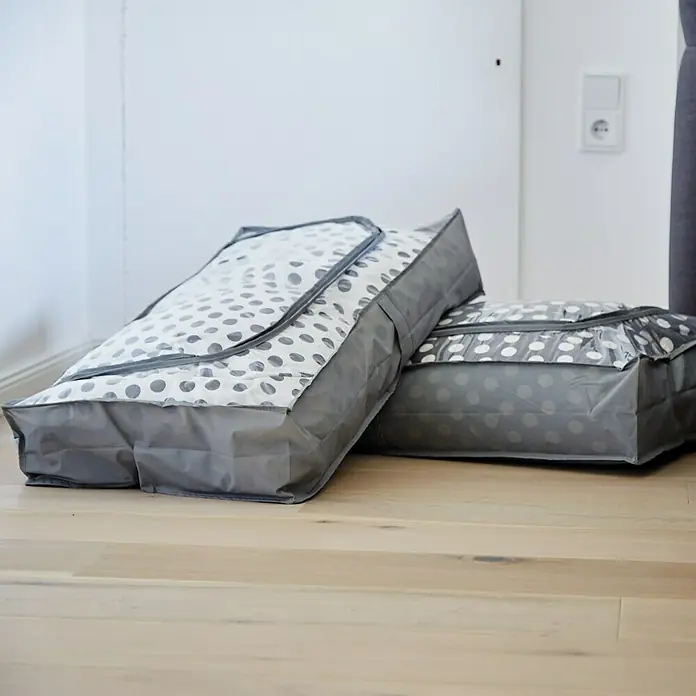 Unterbettkommoden-Set - 90 x 45 x 16 cm, 2 Stk., Polyester - Zwei graue Aufbewahrungsbeutel mit Punktmuster auf einem Holzboden, ideal zur ordentlichen Lagerung von Kleidung und Textilien im Haushalt.