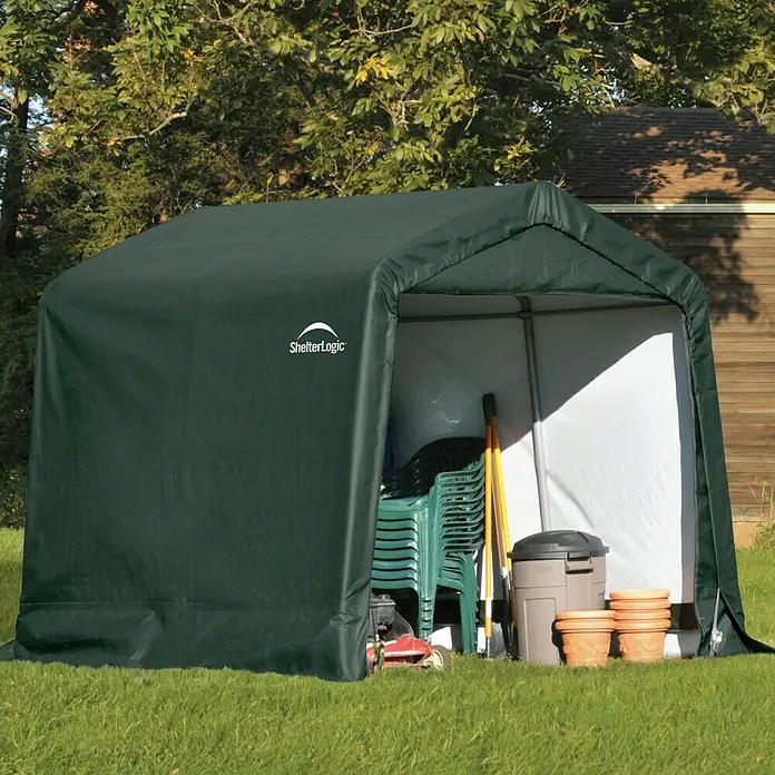 ShelterLogic Gerätehaus - Außenbreite inkl. Dachüberstand: 240 cm, Außentiefe inkl. Dachüberstand: 240 cm, Stahl, Grün - Dunkelgrünes ShelterLogic-Lagerzelt im Garten, gefüllt mit Gartenstühlen und Werkzeugen, ideal für die wettergeschützte Aufbewahrung im Freien.