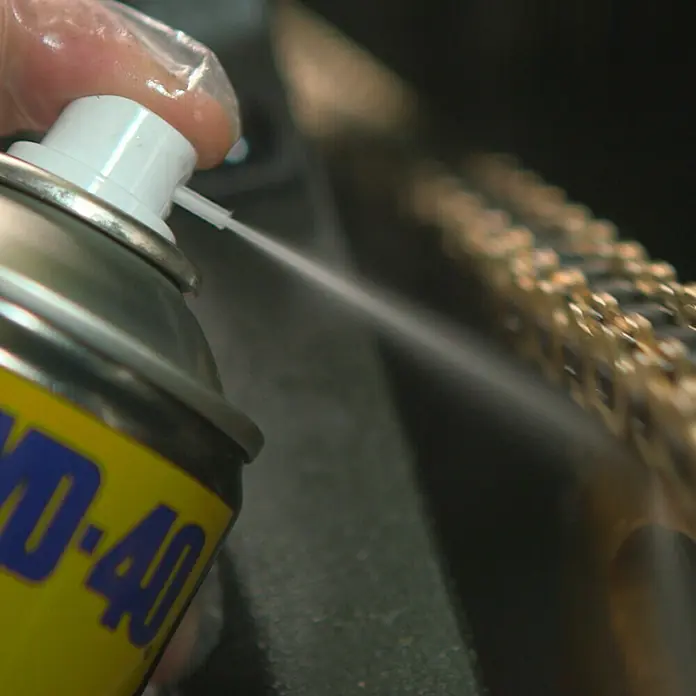 WD-40 Specialist Motorbike Kettenspray - 100 ml, Geeignet für: Ketten - Sprühen von WD-40 auf eine goldene Kette zur Schmierung. WD-40 ist ein vielseitiges Schmiermittel und Rostlöser für verschiedene Anwendungen.