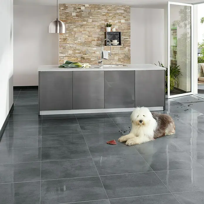 Art-Tec by Palazzo Feinsteinzeugfliese - 30 x 60 cm, Graphit, Matt - Das Bild zeigt eine moderne Küche mit glänzenden grauen Fliesen und einem kuscheligen Old English Sheepdog, der auf dem Boden liegt.