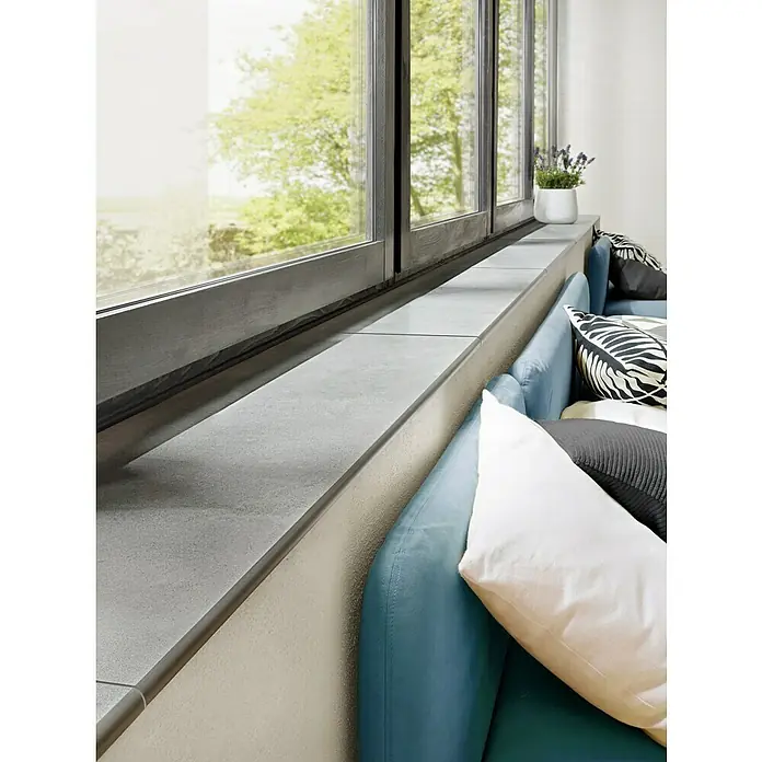 Art-Tec by Palazzo Sockelfliese - 7 x 60 cm, Steel, Matt - Nahaufnahme eines modernen Fensters mit grauen Fensterbänken und einer bequemen blauen Couch mit dekorativen Kissen.