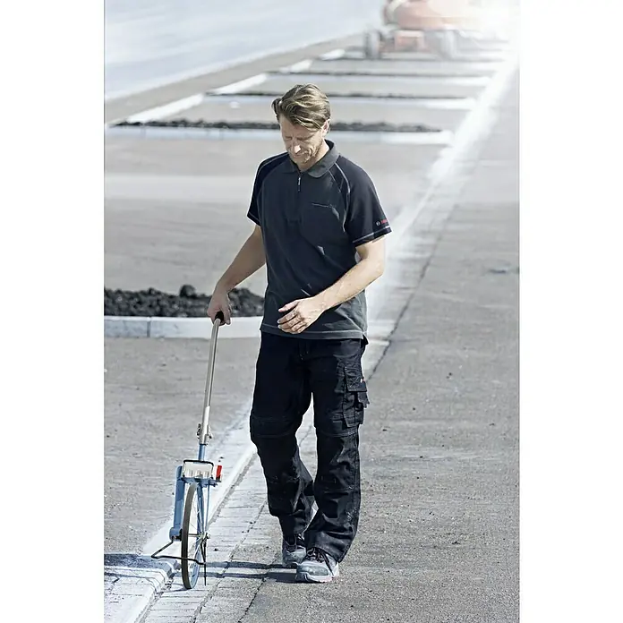 Bosch Professional Messrad GWM 40 - Messbereich: Max. 9999,99 m, Messgenauigkeit: ± 5 cm/100 m - Ein Mann misst eine Straße mit einem blauen Messrad. Er trägt ein anthrazitfarbenes Poloshirt und schwarze Hosen.