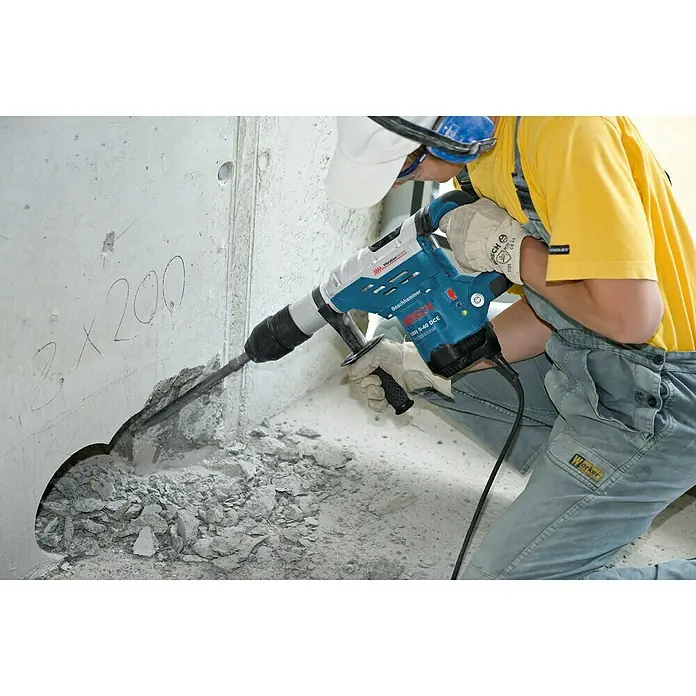 Bosch Professional Martillo perforador GBH 5-40 DCE - 1.150 W, 8,8 J, Alojamiento SDS-MAX - Un trabajador de la construcción usa un martillo demoledor Bosch GSH 5-40 DCE para perforar un agujero en una pared de hormigón.