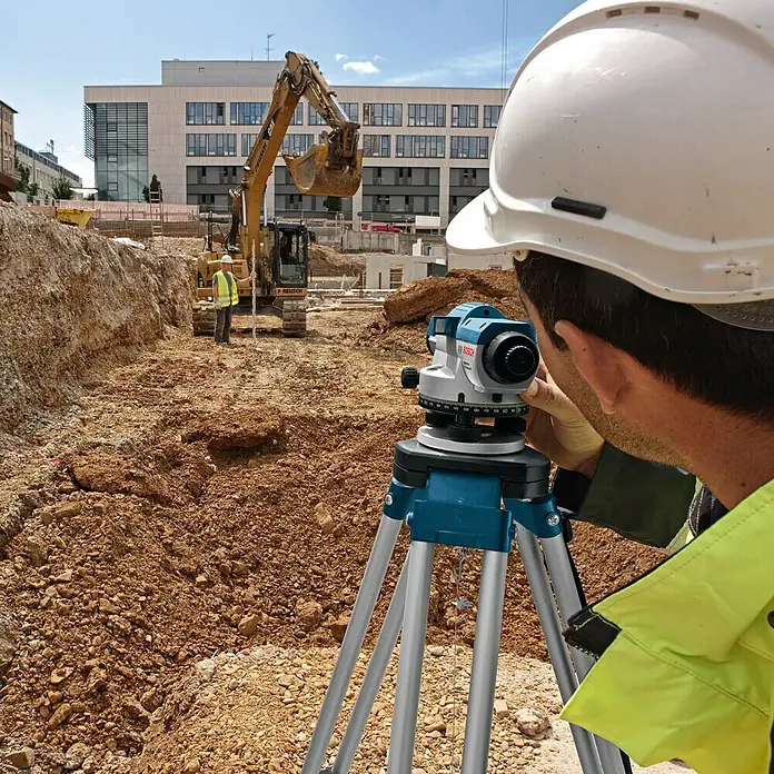 Bosch Professional Optisches Nivelliergerät GOL 20 D - Arbeitsbereich: Max. 60 m, Maßeinteilung: 1 ° (Horizontalkreis) - Ein Bauarbeiter benutzt ein Bosch Nivelliergerät auf einer Baustelle, um präzise Messungen durchzuführen. Das Gerät steht stabil auf einem Stativ.