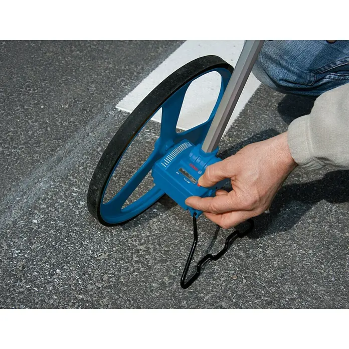 Bosch Professional Messrad GWM 32 - Messbereich: Max. 9999,99 m, Messgenauigkeit: 10 cm/100 m - Nahaufnahme eines Bosch-Messrads, das auf Asphalt verwendet wird, um Abstände genau zu messen.