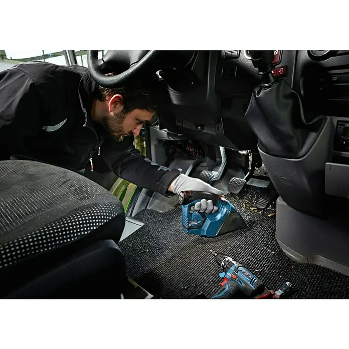 Bosch Professional Akku-Handstaubsauger GAS 12V - 12 V, Li-Ionen, Ohne Akku, Luftmenge: 15 l/s, Karton - Ein Mann benutzt einen Bosch Akku-Staubsauger, um ein Auto zu reinigen. Neben ihm liegt ein blauer Akkuschrauber.