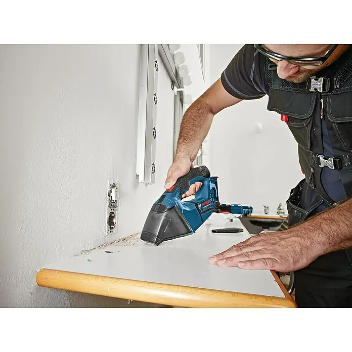 Bosch Professional Akku-Handstaubsauger GAS 12V - 12 V, Li-Ionen, Ohne Akku, Luftmenge: 15 l/s, Karton - Ein Mann reinigt mit einem blauen Bosch Akku-Handsauger eine weiße Oberfläche. Der Sauger ist kompakt und ideal für schnelle Reinigungsarbeiten.