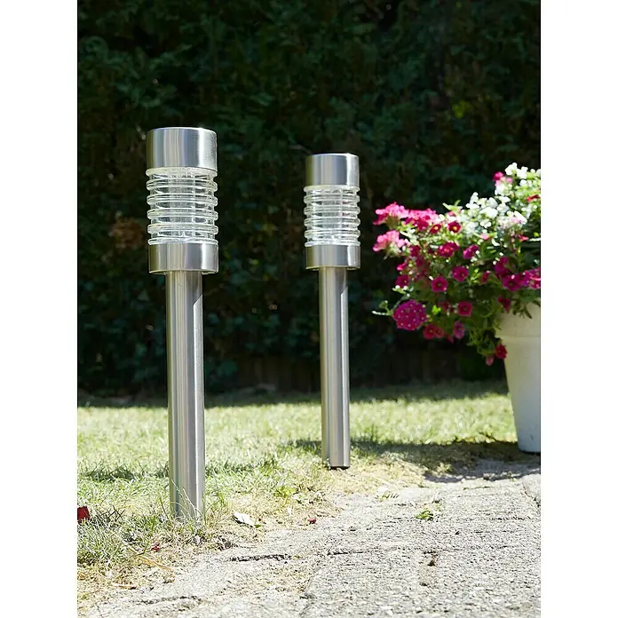 Luxform Solar-Erdspieß Torino - L x B x H: 7,5 x 7,5 x 58 cm, Silber, 8 lm - Nahaufnahme von zwei silbernen Gartenleuchten mit geriffelten Lampenschirmen auf einem Rasen.