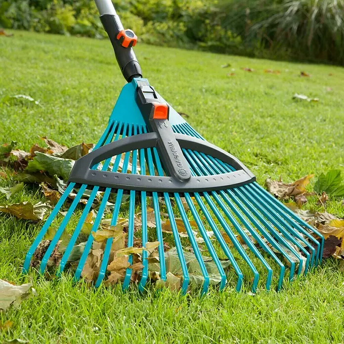Gardena Combisystem Verstellbesen - Arbeitsbreite: 35 cm - 52 cm, Verstellbare Zinken - Der Gardena Rechen liegt auf dem grünen Rasen und ist mit Herbstlaub bedeckt. Der Rasenrechen hat verstellbare Zinken für verschiedene Anwendungen.