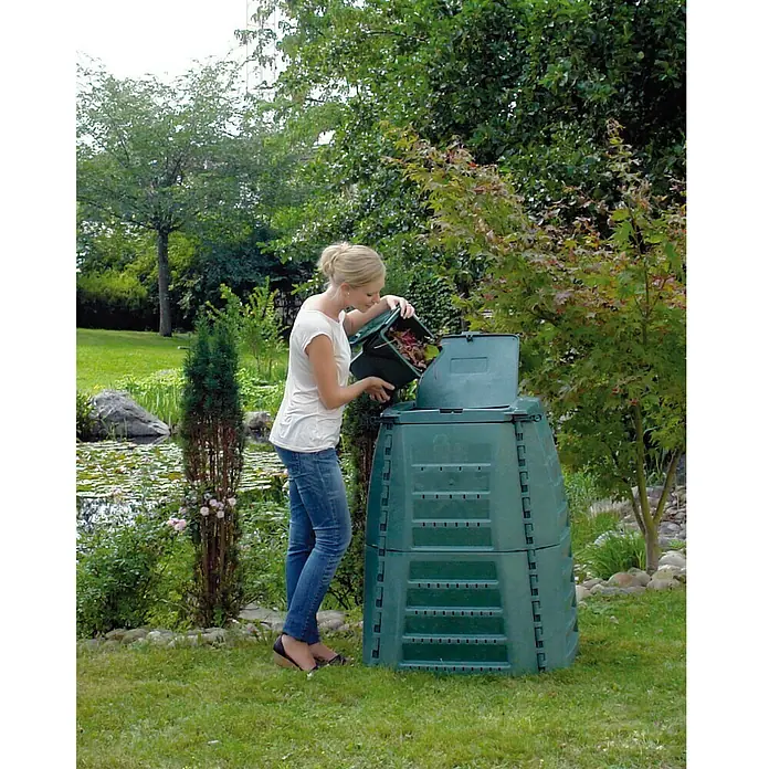 Garantia Komposter Thermo Star - 1.000 l, 130 x 130 x 102 cm - Eine Frau leert einen grünen Eimer mit organischen Abfällen in einen modularen, grünen Kompostbehälter im Garten.