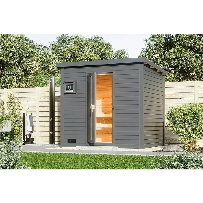 Karibu Saunahaus Hytti - 9 kW Saunaofen mit externer Steuerung, Terragrau, L x B x H: 196 x 231 x 228 cm - Graue Außensauna mit Glastür und Bedienfeld an der Seite, umgeben von Grün. Die Sauna steht auf einer gepflasterten Fläche im Garten.