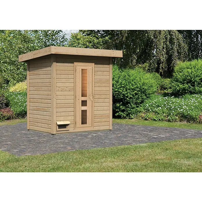 Karibu Saunahaus Hytti - Ohne Ofen, L x B x H: 146 x 196 x 228 cm, Natur - Das Bild zeigt eine Holzsauna im Außenbereich mit einer Tür und einem kleinen Fenster, die auf einer gepflasterten Fläche in einem Garten steht.