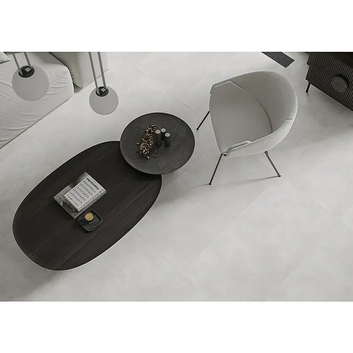 Feinsteinzeugfliese Big Show XXL - 59,8 x 119,8 cm, Weiß, Matt - Blick von oben auf ein modernes Wohnzimmer mit grauem Sessel, Couchtisch und Dekoration, das ein stilvolles und komfortables Ambiente vermittelt.