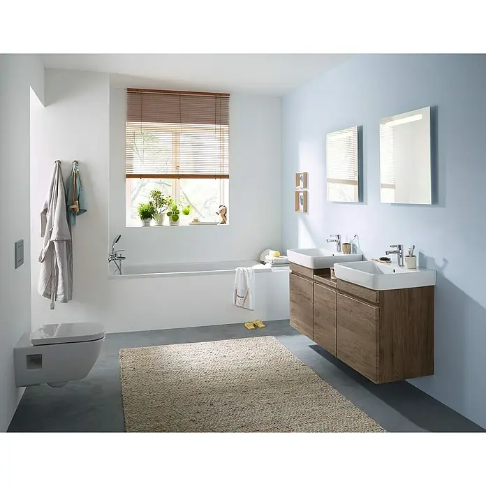 Geberit Renova Plan Wand-WC - Spülrandlos, Ohne Spezialglasur, Spülform: Tief, WC Abgang: Waagerecht, Weiß, Teilgeschlossenes Design - Ein modernes Badezimmer mit zwei Waschbecken auf Holzunterschränken, einem WC und einer Badewanne. Braune Jalousien filtern das Tageslicht.