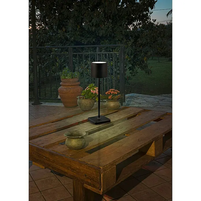 Reality Leuchten Akku-Tischleuchte FERNANDEZ - 1 W, L x B x H: 12,5 x 12,5 x 38 cm, Schwarz, Mehrfarbig - Eine schwarze Tischleuchte auf einem Holztisch im Freien, die eine gemütliche Atmosphäre schafft.