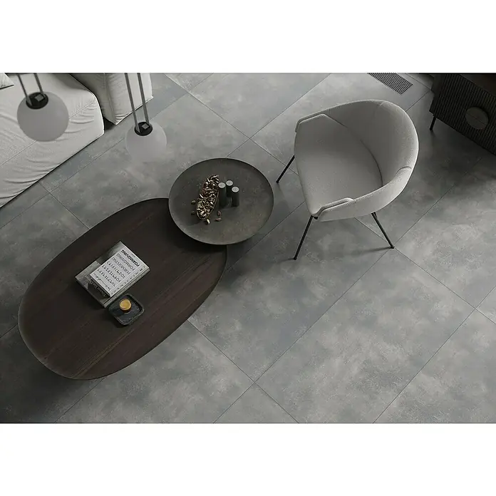 Feinsteinzeugfliese Big Show XXL - 59,8 x 119,8 cm, Grafit, Matt - Modernes Wohnzimmer-Arrangement mit grauem Fliesenboden, Stuhl, Couchtisch und Deko-Elementen. Elegantes Design für stilvolles Wohnen.