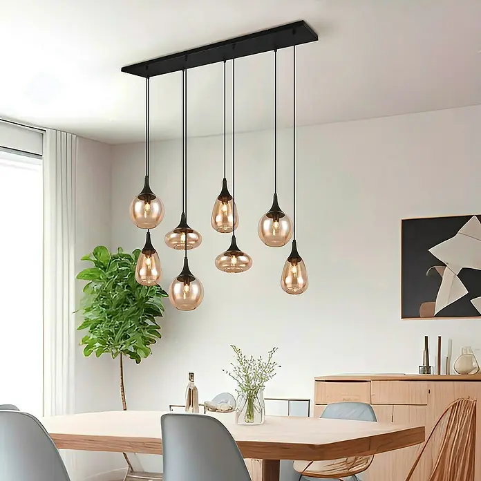 Trio Leuchten Lumina Pendelleuchte - 8 Stk., 320 W, L x B x H: 34,5 x 121 x 150 cm, Amber, Schwarz, E14 - Eine moderne Pendelleuchte mit sieben bernsteinfarbenen Glasschirmen, die über einem Esstisch in einem stilvollen Raum hängen.