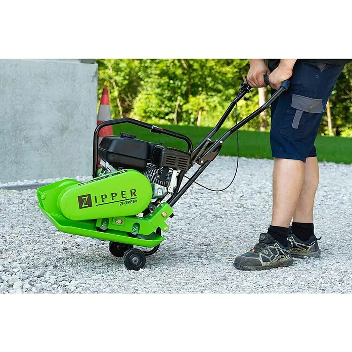 Zipper Rüttelplatte ZI-RPE60 - Motorleistung: 4.100 W, 3,6 l - Aufnahme eines hellgrünen Zipper Vibrationsstampfers ZI-RPE60, der von einer Person auf einem Schotterweg bedient wird.