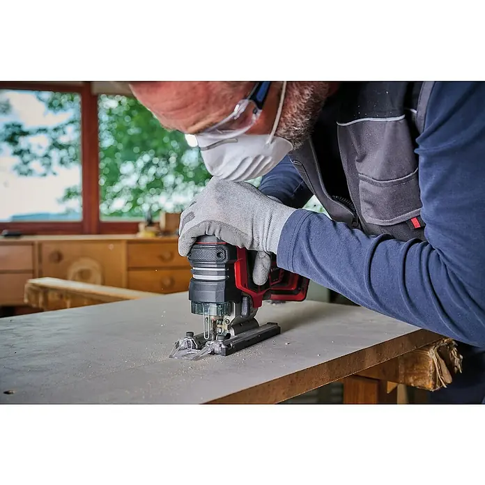 Einhell Professional Power X-Change 18V Akku-Pendelhubstichsäge TP-JST 18/135 Li BL - Solo - 18 V, Li-Ionen, Ohne Akku - Nahaufnahme einer Stichsäge in Aktion, bedient von einem Handwerker mit Schutzmaske und Brille, der ein Werkstück bearbeitet.