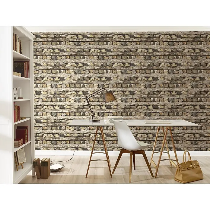 Rasch Vliestapete Holzstapel - Braun, Holzoptik, 10,05 x 0,53 m - Einrichtungsidee mit einer weißen Bücherregal, einem Tisch mit Lampe und einem Stuhl vor einer Backsteinmauer. Die Ledertasche rundet den Look ab.