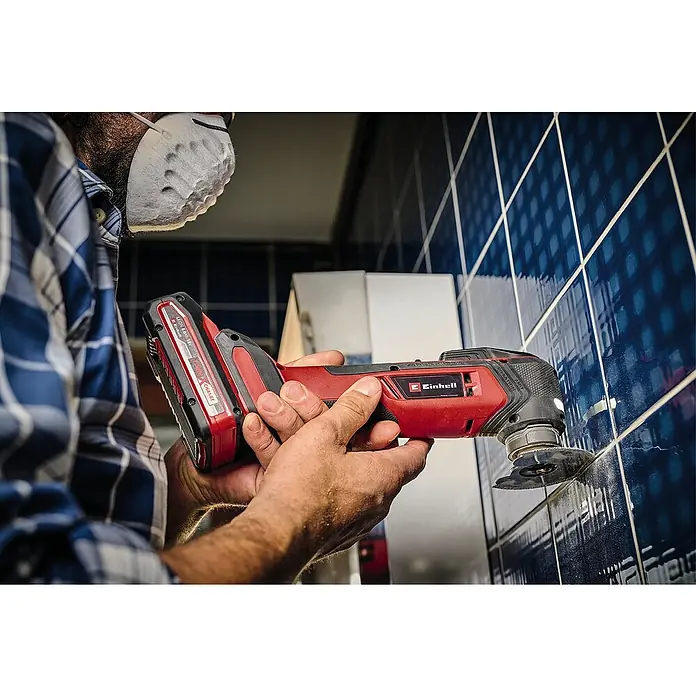 Einhell Professional Power X-Change 18V Akku-Multifunktionswerkzeug TP-MG 18 Li BL-Solo - 18 V, Ohne Akku, Oszillationswinkel: 3,2 ° - Ein Mann verwendet einen Einhell Akku-Multifunktionsschneider zum Schneiden von Fliesen. Das rote Werkzeug ist mit einem Akku ausgestattet.