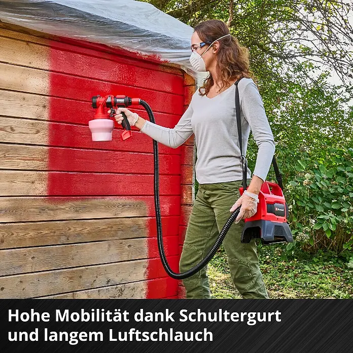 Einhell Power X-Change 18V Akku-Farbsprühsystem Akku-Farbsprühsystem TE-SY 18/90 Li-Solo - 18 V, Ohne Akku - Frau streicht mit Einhell Farbsprühsystem ein Holzhaus rot an.