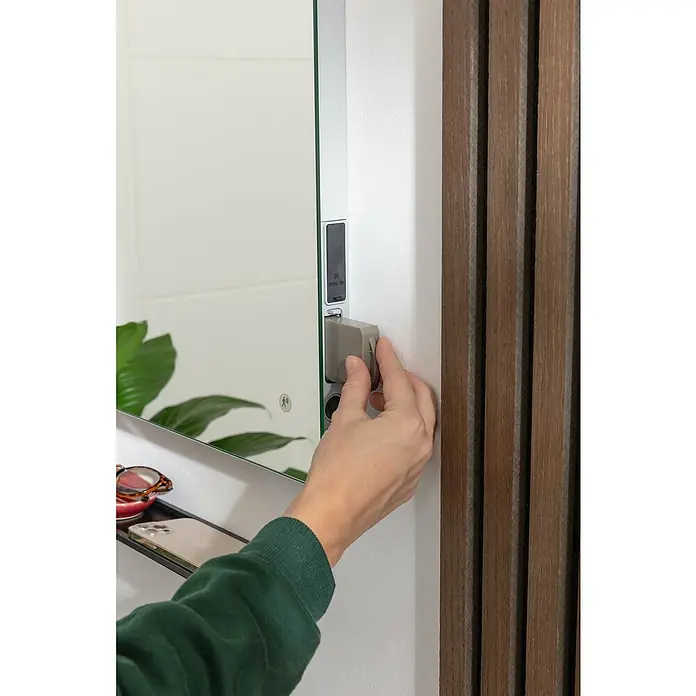 Camargue Lichtspiegel Akku - 50 x 70 cm, Mit Lithium-Ionen Sekundärbatterie - Ein beleuchteter Spiegelschrank mit einer Hand, die eine graue Steckdose bedient. Das elegante Design umfasst ein Regal für Accessoires.
