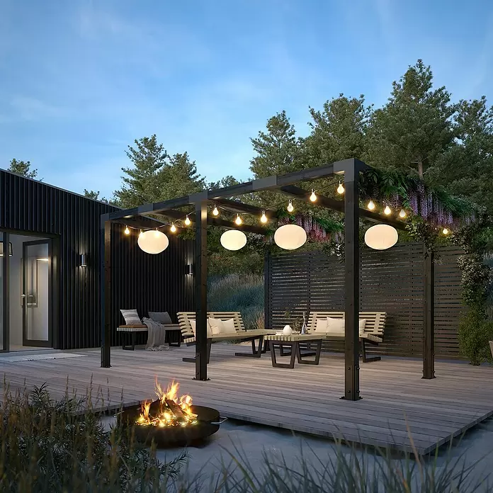 Plus Pergola Cubic - L x B x H: 387 x 387 x 217 cm, Holz, Schwarz RAL 9005, Inkl. Tokyozäunen - Ein einladender Gartenbereich bei Dämmerung mit dunkler Pergola, Lichterketten, Holzterrasse, Sitzgelegenheiten und Feuerstelle.