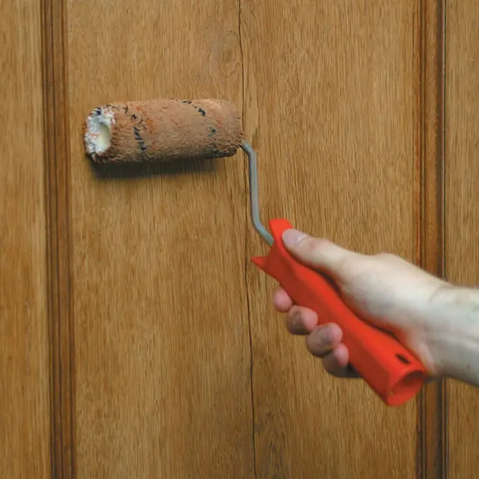 Lehnartz Holzschutzroller Komplett-Set - 4 -tlg., Geeignet für: Lasuren - Eine Nahaufnahme eines Farbauftrags mit einer Farbwalze auf einer Holztür, die zeigt, wie die Farbe aufgetragen wird und das Holz schützt.