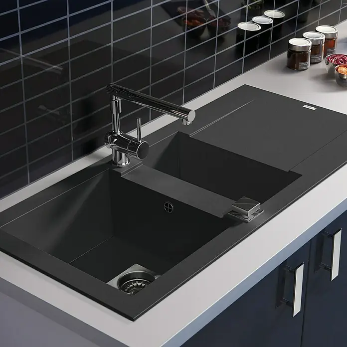 Carea Einbauspüle Dukkah - 105 x 50 cm, Schwarz, Material Spüle: CAREAgranit® - Nahaufnahme einer modernen schwarzen Küchenspüle mit einem verchromten Wasserhahn und einem Abtropfbereich, eingebaut in eine Arbeitsplatte.