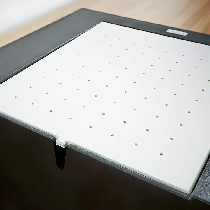 Carea Fregadero encastrable Eole - 50 x 47,6 cm, Negro - Primer plano de un panel brillante y perforado, probablemente parte de un dispositivo o accesorio, enmarcado por un entorno gris oscuro.