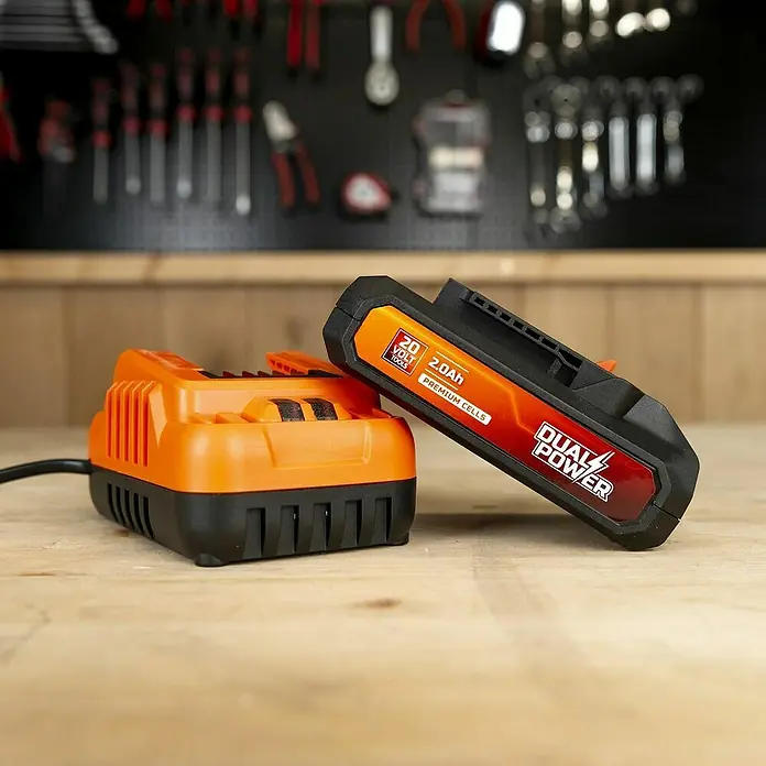 PowerPlus Batería y cargador POWDP90620 - 20 V, 1 batería, 2 Ah - Primer plano de un cargador de batería Dual Power naranja y una batería de 2,0 Ah, colocados en un banco de trabajo de madera.